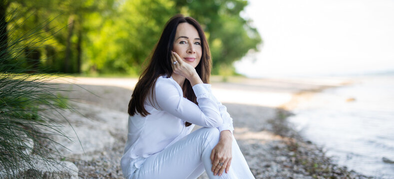 Attraktive und sympathische Frau in weißer Bluse an einem See, Schönheit und Entspannung 