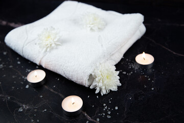 A white towel lies on a dark background surrounded by white flowers and burning candles. High quality photo