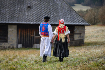A couple dressed in traditional folk costume. Slovak costume in autumn nature. Old country cottage in the background. Young couple in folk costume walking in the garden