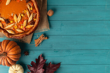 top view of pumpkin pie on wooden turquoise background decorated with autumn leaves and pumpkin - obrazy, fototapety, plakaty