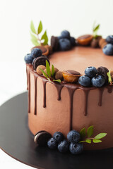 Brown birthday chocolate cake decorated with bluberries, candies and chocolate drips on top. White background.
