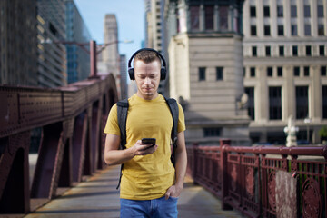Young man listening to music with wireless headphones and looking into his cell phone during city...