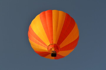 Looking up at a bright orange and yellow hot air balloon flying in the sky