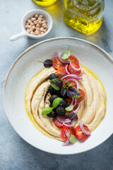 Hummus with tomato salad served in a beige plate, vertical shot on a light-blue stone background