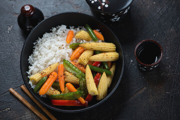 Rice bowl with vegetable stir-fry on a dark-brown stone background, elevated view, horizontal shot