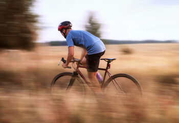 Cyclist in motion. Young sporty man rides gravel bike along the trail in the field. Blurred motion....