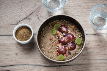 Bowl of flaxseed porridge served with sliced grapes, high angle view on a brown wooden background, studio shot