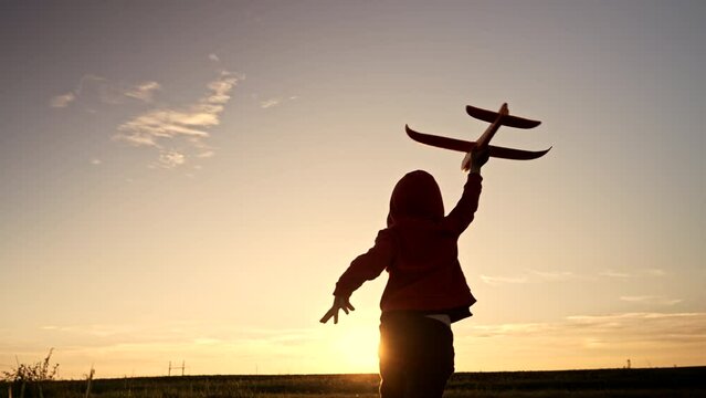 Silhouette of happy little boy running with toy plane or aircraft on sunset sky background. Child playing with airplane, he wants to become aviator in future. Amazing footage, fun, game concept.