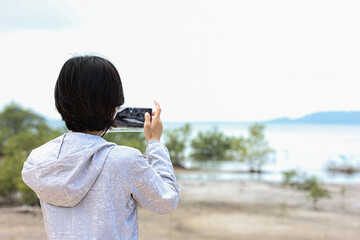 Asian woman use smartphone taking sea view and roadside photos in southern Thailand. Travel vacation concept.	