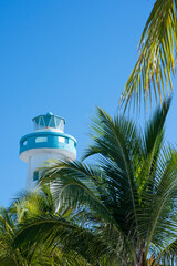 Vertical view of a lighthouse tower against the blue sky, and coconut palms in Isla Mujeres, Mexico