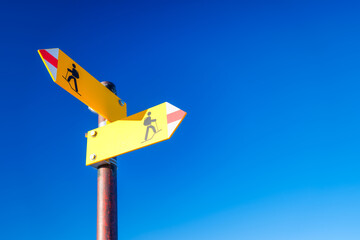 Directional marker for a mountain hike. Yellow bright sign with an arrow against the blue sky. Navigation in a hiking trip.
