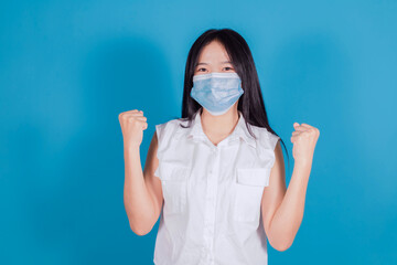 Asian woman in medical face mask to protect Covid-19 (Coronavirus) raise hands glad excited cheerful on blue background