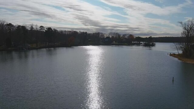 gorgeous aerial footage of the rippling waters of the Catawba River at sunset with the sun reflecting off the water surrounded by lush green trees and autumn colored trees with blue sky and clouds