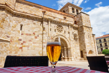 Glass of beer while sightseeing in front of the medieval church of Zamora Spain. - obrazy, fototapety, plakaty