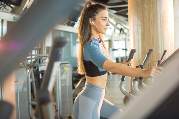 Active young woman exercising on elliptical trainer machine at gym