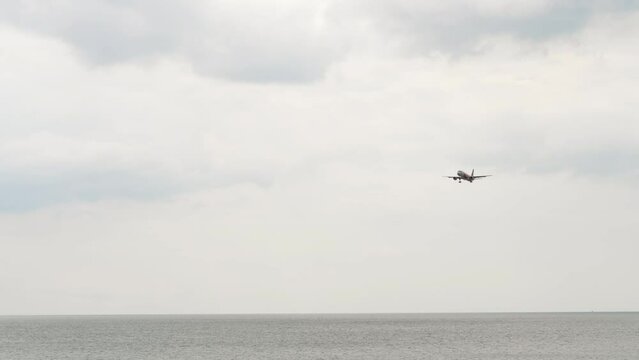 Long shot of airplane approaching to land at Phuket airport. Airplane flies over the ocean. Tourism and travel concept