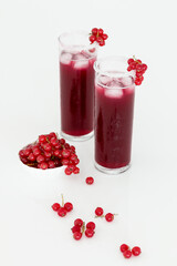 Red currant juice in two tall glasses. There are red currants in a small white bowl next to it. - 508820391