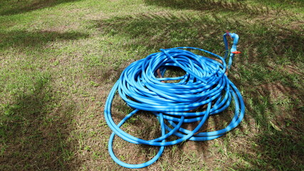 Roll the blue rubber hose on the ground. Flexible plastic garden hose with palm leaf shadow and copy space. Selective focus