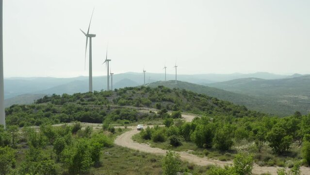 the car goes on the road near the windmills in the mountains. Production of clean environmental energy in nature and people go on a journey.