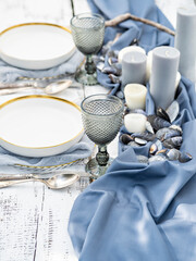 Inspirational image of luxury table setting in marine style with candles, shells. Table served for engagement, wedding, romantic dinner or festive event. Outdoor glamorous catering or dining.