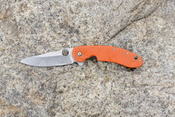 Folding knife everyday carry (EDC) with orange handle on stone backgound. Blade with water drops.