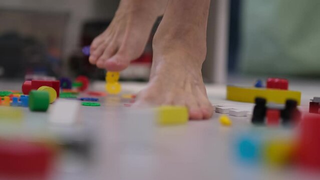 barefoot man walks among the scattered toys. Foot stepping on children's toys. Scattered toys on the floor.