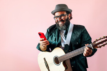 Happy bearded man using smartphone with acoustic guitar.