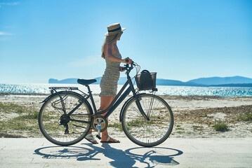 Fototapeta premium Carefree woman with bike riding on sand beach having fun, on the seaside promenade on a summer day.