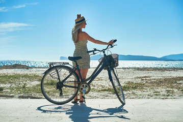 Obraz premium Carefree woman with bike riding on sand beach having fun, on the seaside promenade on a summer day.