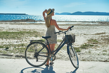 Naklejka premium Carefree woman with bike riding on sand beach having fun, on the seaside promenade on a summer day.