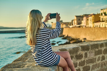 Woman traveler tourist using smartphone, taking photo of sea view at sunset in summer day. Enjoying European, Famous popular touristic place in world.

