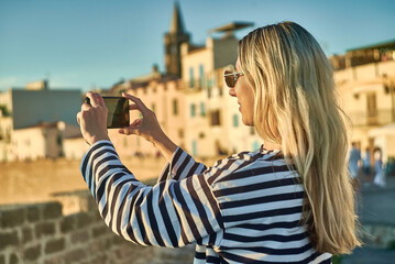 Woman traveler tourist using smartphone, taking photo of sea view at sunset in summer day. Enjoying European, Famous popular touristic place in world.
