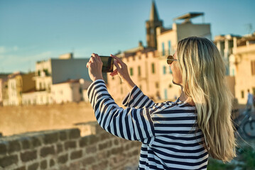 Woman traveler tourist using smartphone, taking photo of sea view at sunset in summer day. Enjoying European, Famous popular touristic place in world.
