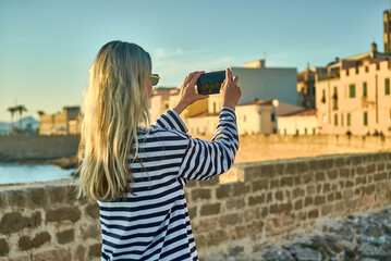 Woman traveler tourist using smartphone, taking photo of sea view at sunset in summer day. Enjoying European, Famous popular touristic place in world.
