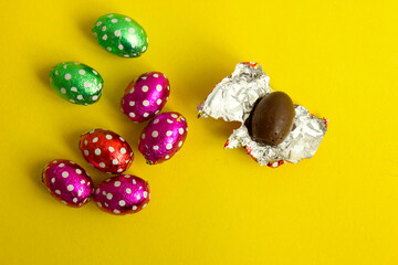 Chocolate egg in colorful foil for Easter on yellow background. The egg is wrapped in red foil. Happy Easter. Chocolate. Sweets for children and adults. Candy. Dessert. Copy space. Top view. Flat lay