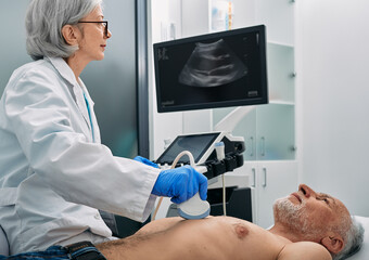 Heart ultrasound exam for senior man with ultrasound specialist while medical exam. Heart health exam with ultrasound scan machine - Powered by Adobe