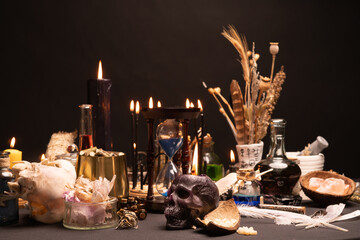 Selective focus on human skull candle. Occult and esoteric witch doctor still life. Halloween with magic objects. Black candle, crystal stones, teeth potions bottles on witch table. Mystic witchery.
