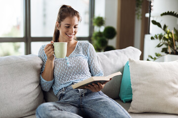 Happy woman reading a book while relaxing on sofa at home