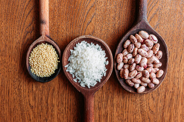 White rice, pinto beans and proso millet seeds on wooden kitchen spoons.