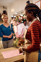 Black florist making flower arrangement for her customer at flower shop.