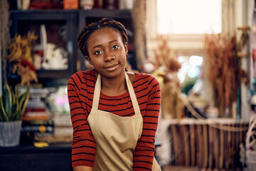 Young African American woman working at flower shop and looking at camera.