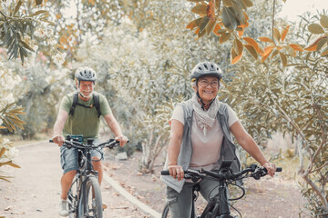 Two happy old mature people enjoying and riding bikes together to be fit and healthy outdoors....