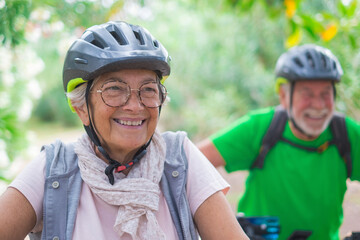 Portrait of one old woman smiling and enjoying nature outdoors riding bike with her husband laughing. Headshot of mature female with glasses feeling healthy.