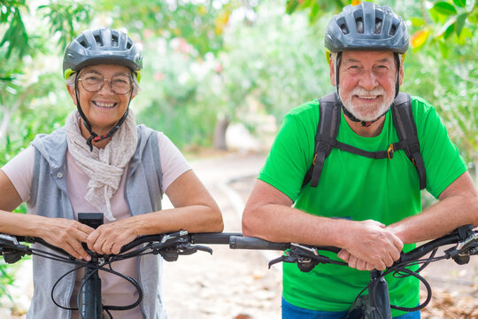Portrait of couple of old and happy in love seniors looking at the camera smiling and having fun with their bikes in the nature outdoors together feeling good and healthy..