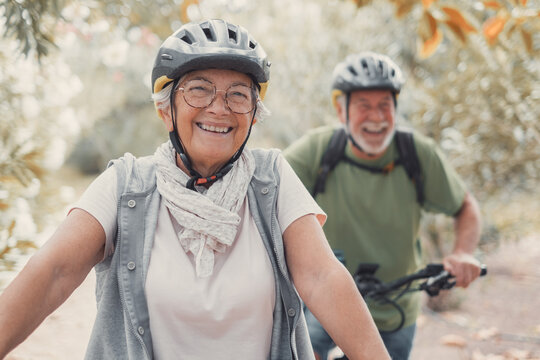 Portrait of one old woman smiling and enjoying nature outdoors riding bike with her husband laughing. Headshot of mature female with glasses feeling healthy. Looking at the camera