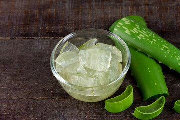 Aloe vera gel in transparent glass bowl with fresh aloe vera on rustic wooden background.