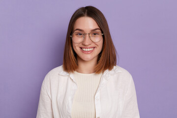 Fototapeta premium Portrait of beautiful smiling satisfied woman wearing white shirt posing isolated over purple background, looking at camera, expressing positive emotions.