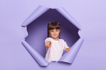 Portrait of serious little girl with pigtails wearing striped shirt breaks through purple paper...