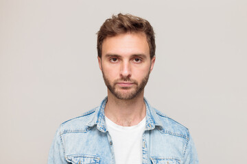Young hipster male with stubble in a white t-shirt and light blue denim shirt. Emotion - disappointment, no mood, despair. On a light gray background - obrazy, fototapety, plakaty
