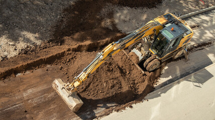 yellow excavator digs a hole at a construction site, top view